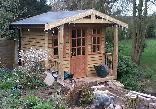 A Warwick Buildings Summer Room in Feather Edge Cladding. Featuring end posts which support the overhang on the front gable end and balustrade infil to each side